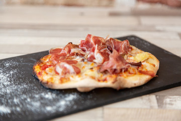 Close up of ham pizza on a blackboard on a wooden table
