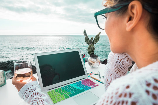 free digital nomad woman at work with a laptop sitting in front of the ocean in free outdoor space like alternative kind of closed office. Working with technology in nature with freedom for people