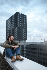 Fototapeta na wymiar Happy bearded hipster looking at the city from roof of building.