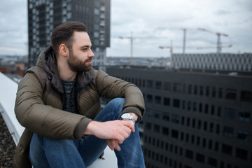 Modern bearded hipster looking at the city from roof of building.