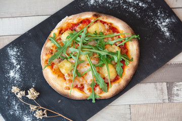 Top view of pizza with arugula on a blackboard garnish with flour