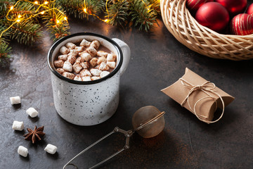 A cup of hot chocolate with marshmallow, fir-tree  branches, Christmas decor and spices. Close up, Selective focus on dark concrete background