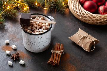 A cup of hot chocolate with marshmallow, fir-tree  branches, Christmas decor and spices. Close up, Selective focus on dark concrete background