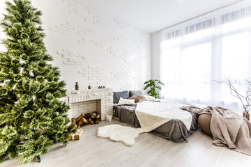 The bedroom decorated by Christmas. Cozy light interior: plaid, wooden bed In the room there is a New Year's fir-tree decorated with toys and garland