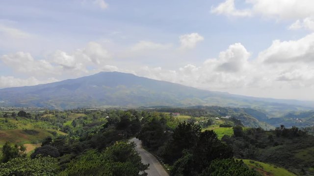Drone shot of over a road full of pines and a background of the active volcano Mt. Kanlaon int he Philippines