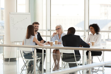 Smiling diverse employees group talking sit at meeting table in modern space conference room, happy...