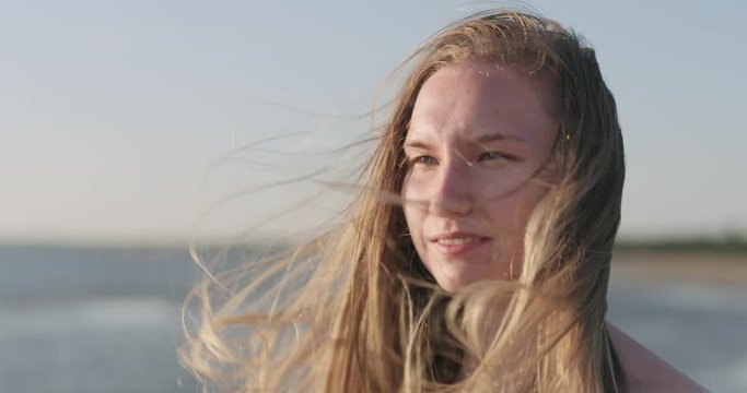 Slow motion closeup portrait of young girl standing on a beach and wind blows her hair