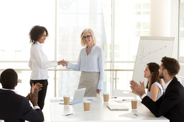 Smiling mature boss handshake millennial african female employee congratulating with promotion,...