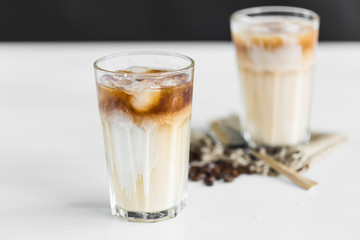 Ice coffee in a glass with cream over and coffee beans on the table