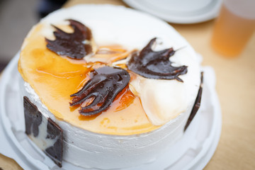 Round white cake with delicate scalded cream, decorated with chocolate pieces of different shapes