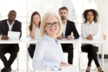 Smiling senior mature woman job applicant looks at camera at interview with hr recruiting team, happy middle aged lady business coach or vacancy candidate portrait, getting hired, employment concept