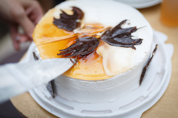 A woman begins to cut with a knife a round white cake, decorated with chocolate pieces of different shapes