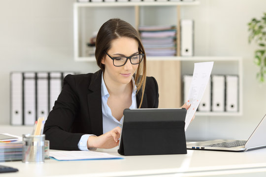 Office worker comparing report with tablet content