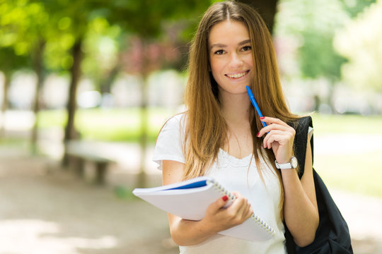 Female student holding a book outdoor in the park and smiling