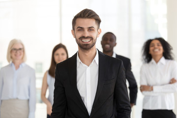 Obraz premium Smiling excited young businessman in suit looking at camera posing with diverse team, millennial professional manager, corporate leader, successful executive, happy ceo or business coach portrait