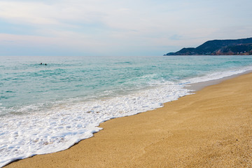 Waves with foam hitting sand on Kleopatra beach in Alanya, Turkey on a sunset against a cloudy sky.  