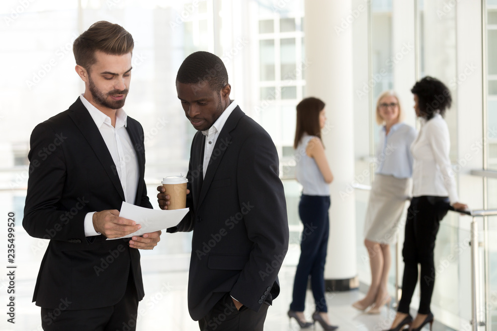 Wall mural Diverse partners colleagues discussing paper, considering contract, reading document, african and caucasian male coworkers talking at work having business conversation about corporate paperwork