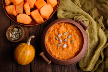 Tasty pumpkin porridge and pumpkins on wooden table.  Pumpkin porridge in a pot. Healthy vegetarian meal