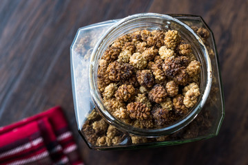 Jar of Dried Mulberries on Dark Wooden Surface.