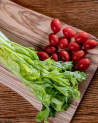Fresh celery and tomatoes on a cutting board on a rustic wooden table