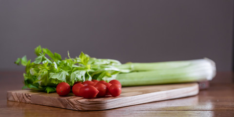 Fresh celery and tomatoes on a cutting board on a rustic wooden table