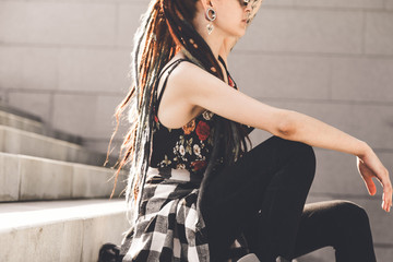 Fototapeta na wymiar young girl with tattoo and dreadlocks sitting on the steps
