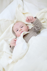 Baby boy in white sunny bedroom. Newborn child relaxing in white bed. Nursery for children. Textile and bedding from bio cotton for kids. New born kid with bio cotton blanket.