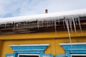 Фрагмент старого сельского дома со снегом на крыше и свисающими сосульками!