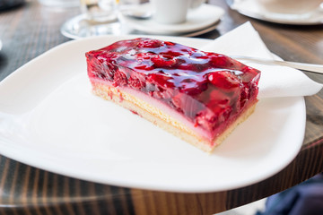 Slice of cake with red berries on a white plate and a wooden table.