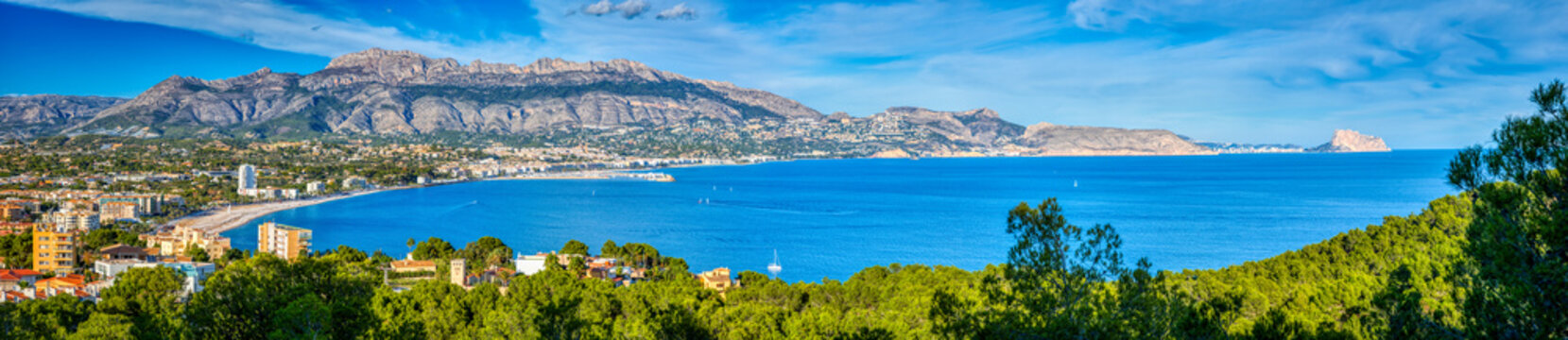 A panoramic view of Altea and the Costa Blanca from the Natural Park Serra Gelada with a bright blue ocean and sky and the mountains and towns of the surrounding area and the green trees of the park