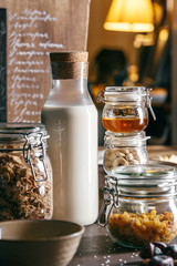 Ingredients for a healthy breakfast stand in different jars on a wooden table. Ingredients: milk, muesli, nuts, honey, raisins.