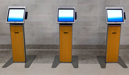 Three freestanding computer kiosks in airport terminal.