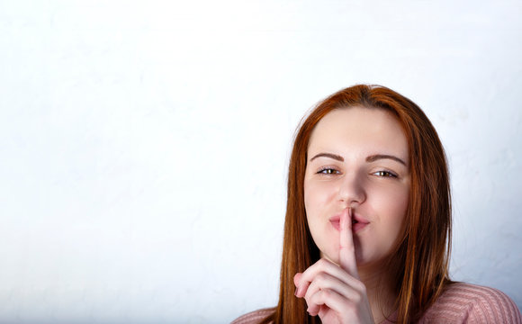 Portrait of young woman keeping finger on her lips and asking to keep quiet, isolated over gray background, Copyspace in left side