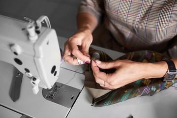 Tailor workplace: view from above of electrical sewing machine and close-up of female hands with needle stitching together garment details before sewing. Handmade exclusive fashionable clothes making.