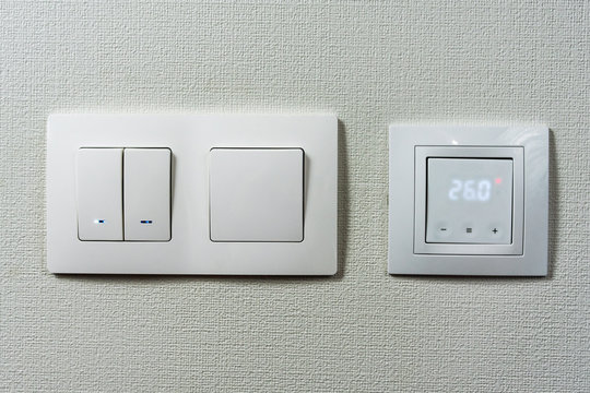  Electric light switch and socket on the empty wall, electrical power socket and plug switched. Comfort house. the sensor for floor heating shows the temperature