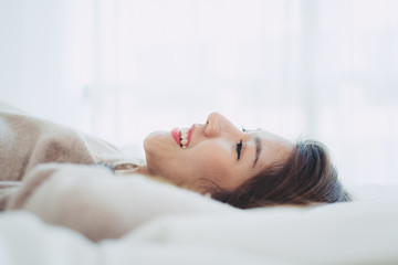 Obraz na płótnie Canvas Portrait beautiful young Asian woman on bed at home in the morning. Cheerful Asian woman wearing a comfortable sweater and smiling on her bed. Relaxing room. lifestyle asia woman at home concept.
