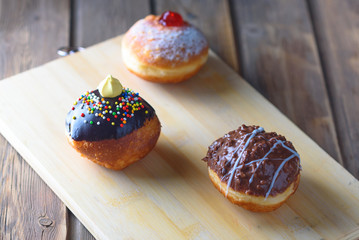 Close up view of tasty various donuts on wood background. Hanukkah celebration concept. Round jelly or jam doughnut sufganiyot and chocolate sufganiyah for Chanukah Jewish holiday.