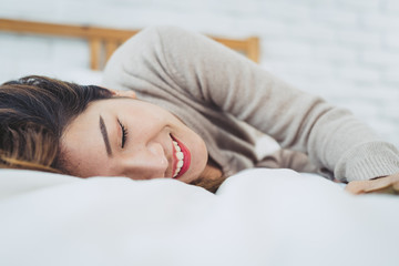 Portrait beautiful young Asian woman on bed at home in the morning. Cheerful Asian woman wearing a comfortable sweater and smiling on her bed. Relaxing room. lifestyle asia woman at home concept.