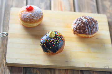 Close up view of tasty various donuts on wood background. Hanukkah celebration concept. Round jelly or jam doughnut sufganiyot and chocolate sufganiyah for Chanukah Jewish holiday.