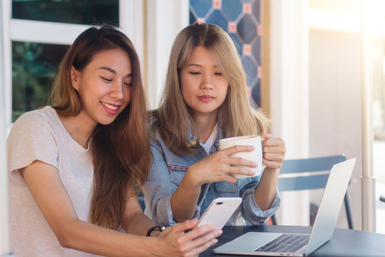 Asian young women working on laptop using and looking smartphone and drinking coffee while sitting in cafe. Lifestyle women communication and working in coffee shop concept.