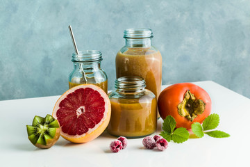 different glasses with freshly made grapefruit, kiwi, persimmon and raspberry smoothies. on white table and blue background. healthy food. morning breakfast