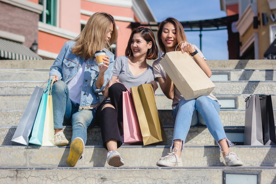 Group of young Asian woman shopping in an outdoor market with shopping bags in their hands. Young Asian women show what they got in shopping bag under warm sunlight. Group outdoor shopping concept.