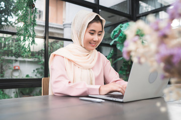 Beautiful young smiling asian muslim woman working on laptop sitting in living room at home. Asian business woman working document finance and calculator in her home office. Enjoying time at home.