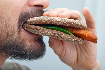 Man bites sandwich with rye bread and sausage
