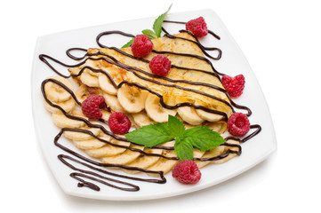 Crepes with chocolate cream, banana and raspberries on white background.