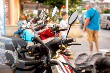 New motorcycles and mopeds exhibited for sale on the street near the store. The man is interested.