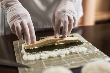 Close-up view of process of preparing rolling sushi with nori, rice and omelet on bamboo mat