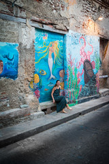 Frau im Kleid sitzt im Künstlerviertel Getseman vor einer Graffitiwand in Cartagena de Indias,...