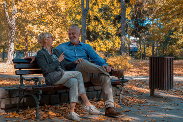 Smiling senior man and woman sitting on a bench and having fun in park