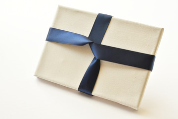 Close up of white canvas wrapped in navy blue ribbon as a gift or present, on white background.  Studio shot